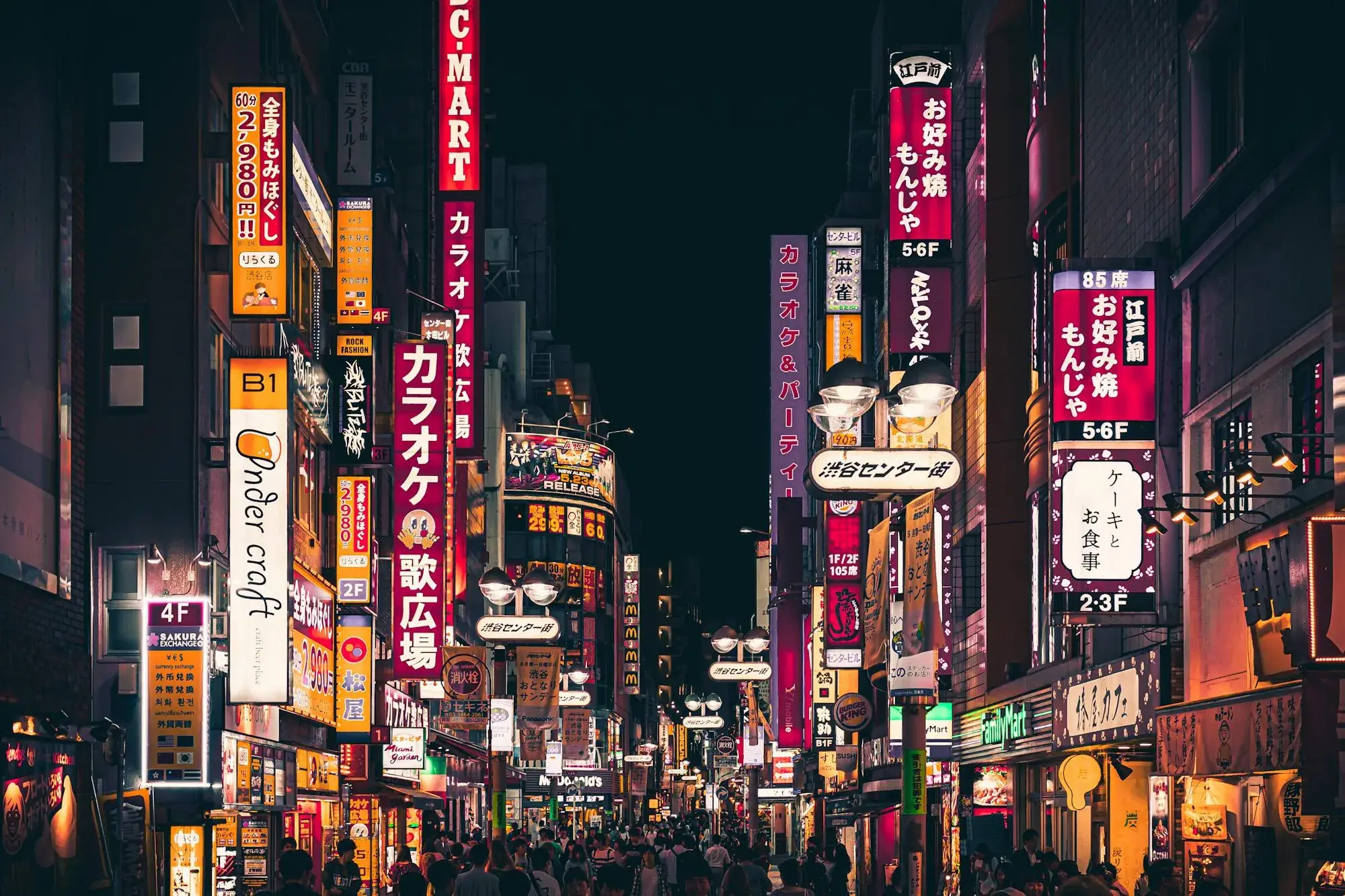 A neon-lit Tokyo street at night, signage in Japanese above shopfronts.