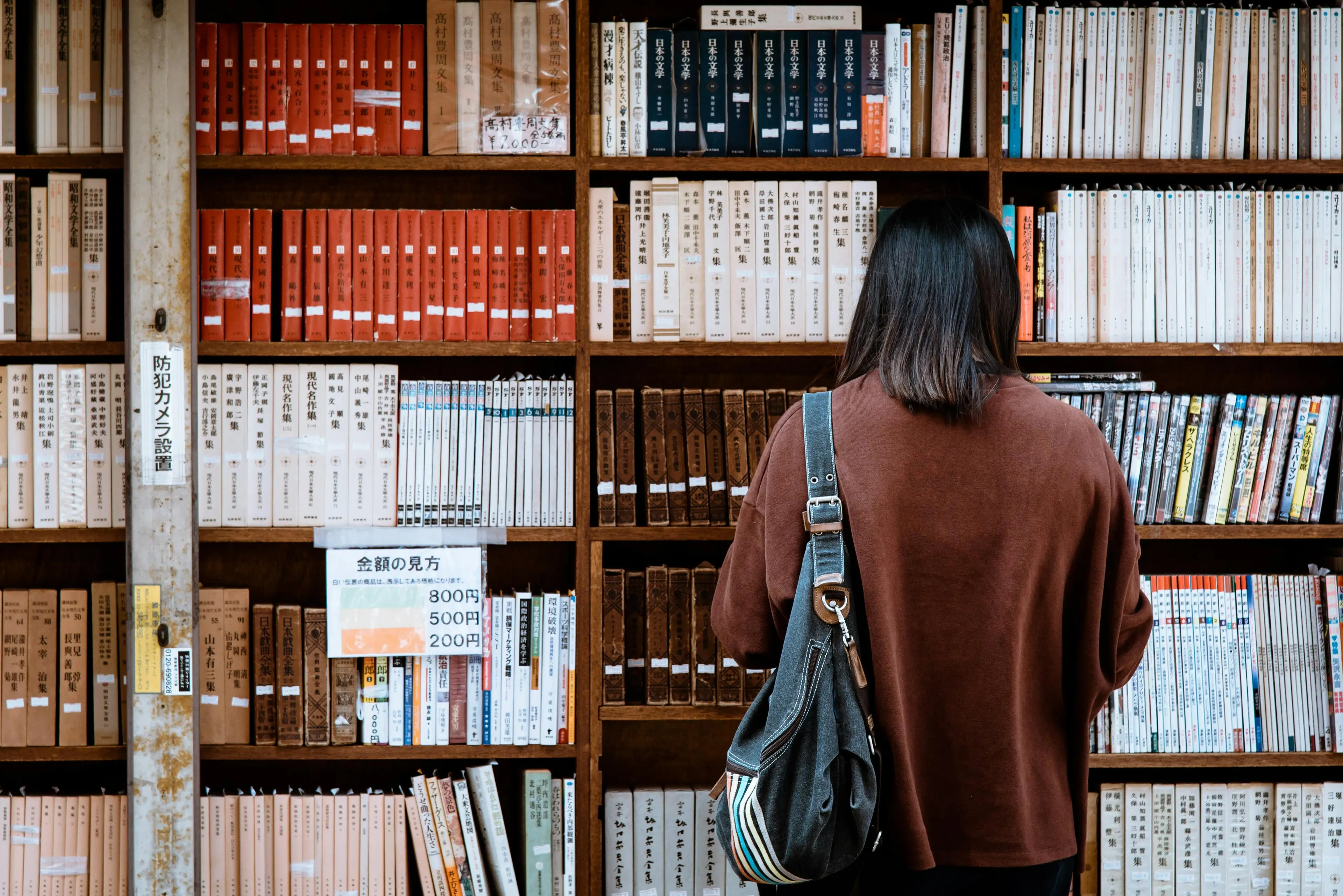 A reader browsing tall shelves of Japanese books in a Tokyo bookshop.